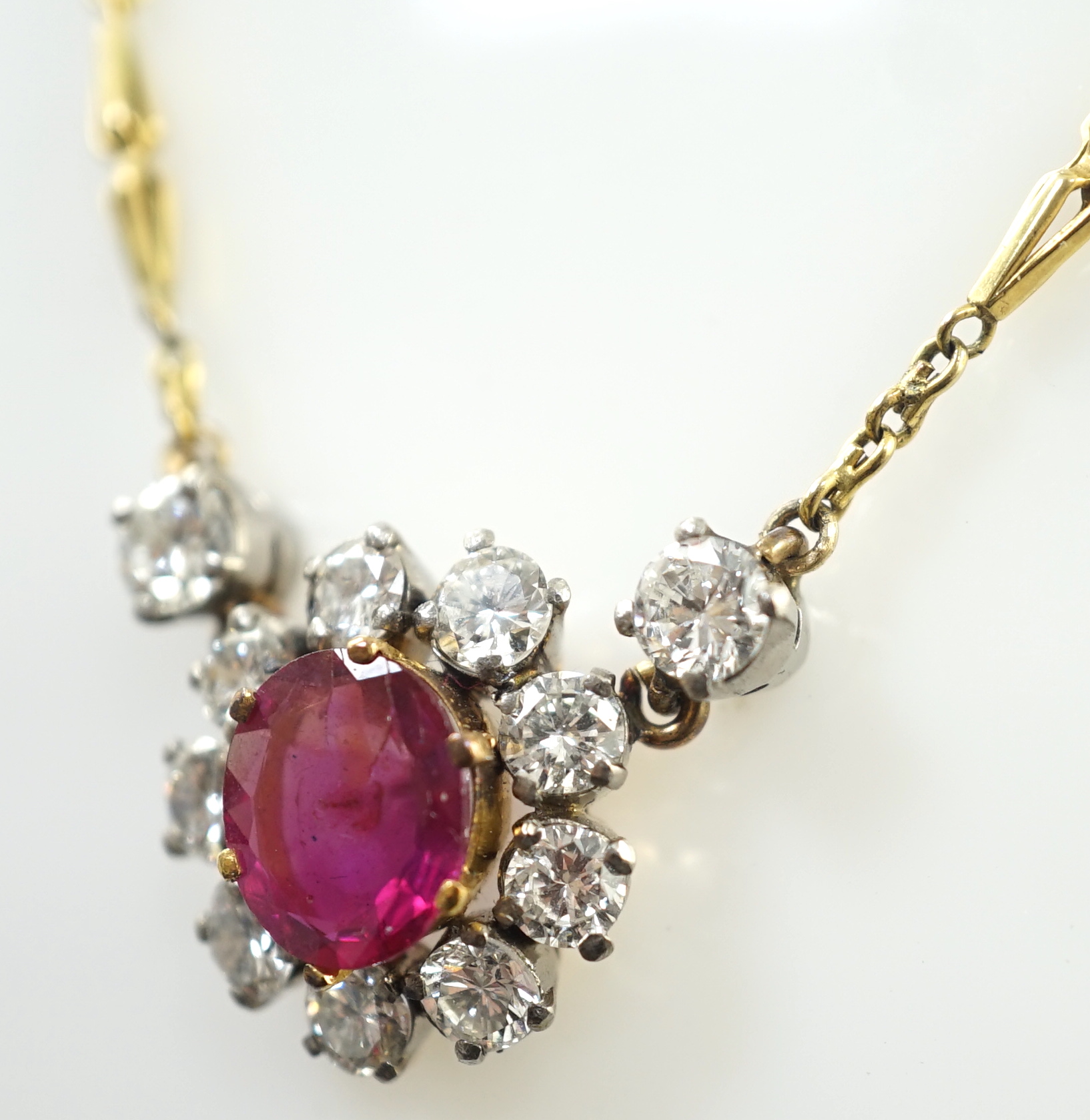 A modern 9ct gold, single stone oval cut ruby and eleven stone round cut diamond cluster set pendant necklace